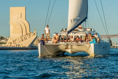 Sinta a brisa num passeio de catamarã ao pôr do sol em lisboa, deguste uma bebida enquanto as luzes da cidade brilham e veja de perto a torre de belém e a ponte 25 de abril. grupo pequeno com bebid