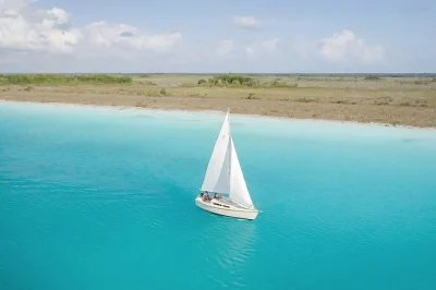 Scivola sulla laguna dei 7 colori di bacalar in barca a vela, con soste per nuotare nei cenote, visitare il canale dei pirati e gustare snack caraibici—include bevande e guida locale.